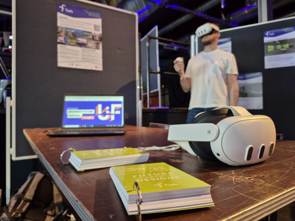 Auf einem Tisch liegen Fächerkarten und eine VR Brille. Im Hintergrund ist eine Person mit einer VR-Brille auf.
